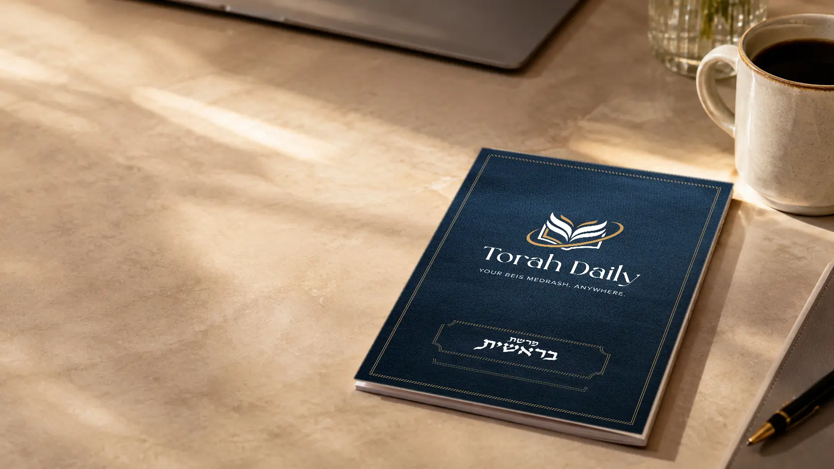 The Torah Daily Bereishis booklet on a desk beside a cup of coffee